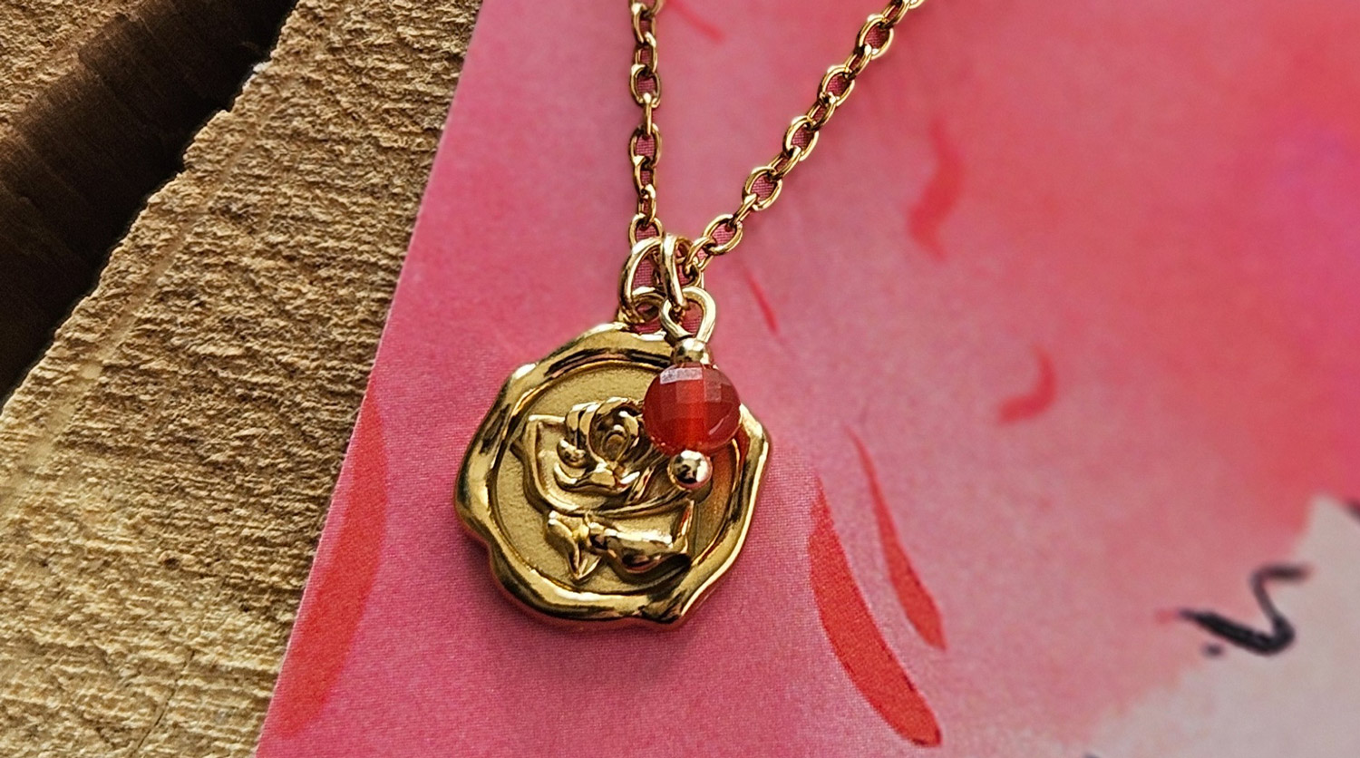 łańcuszek z czerwonym karneolem i metalową zawieszką medalionem w złotym kolorze